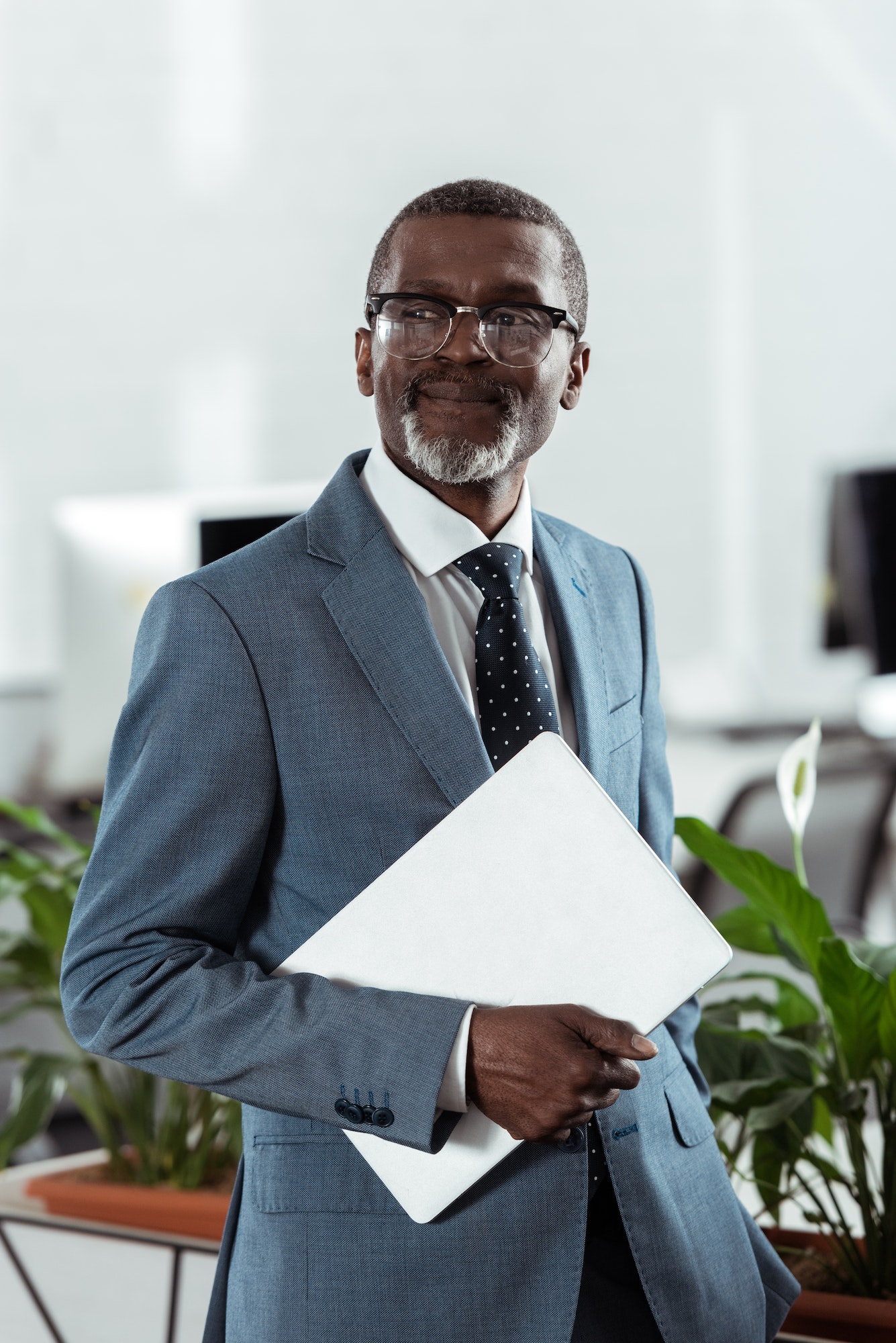 cheerful african american man in glasses holding laptop in office